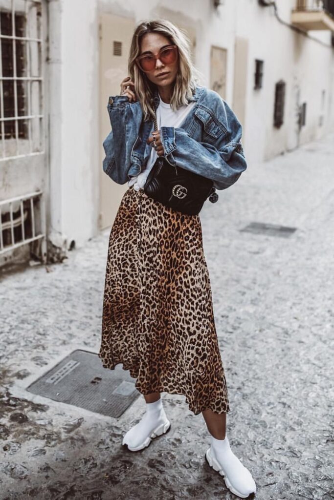 woman in animal print skirt, graphic tee, denim jacket, and white sneakers