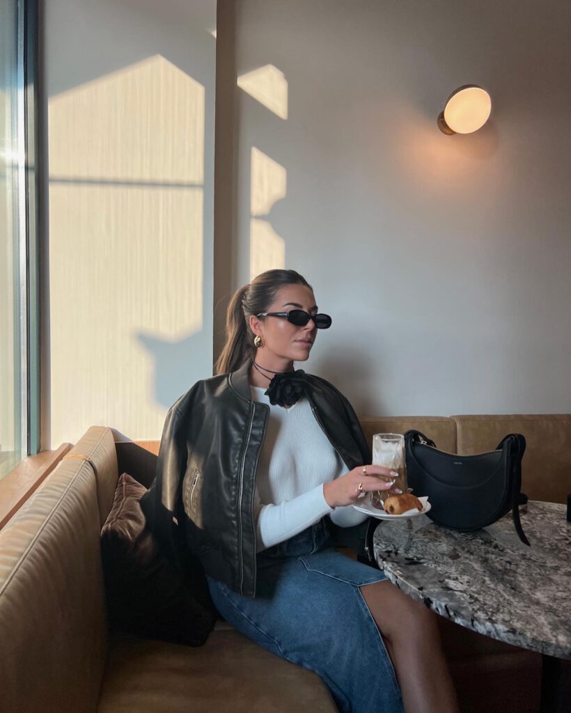 Black leather bomber jacket with a white ribbed top, denim midi skirt and black shoulder bag at a café