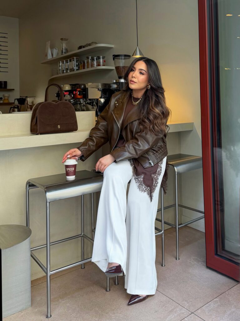 Brown leather moto jacket with a lace-trim brown top, white wide-leg trousers and burgundy heels at a coffee shop