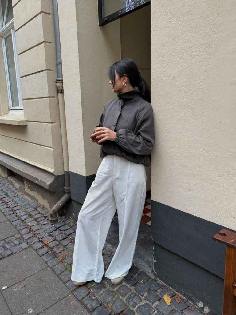 Charcoal high-neck blouse with white wide-leg trousers and sneakers on a cobblestone street