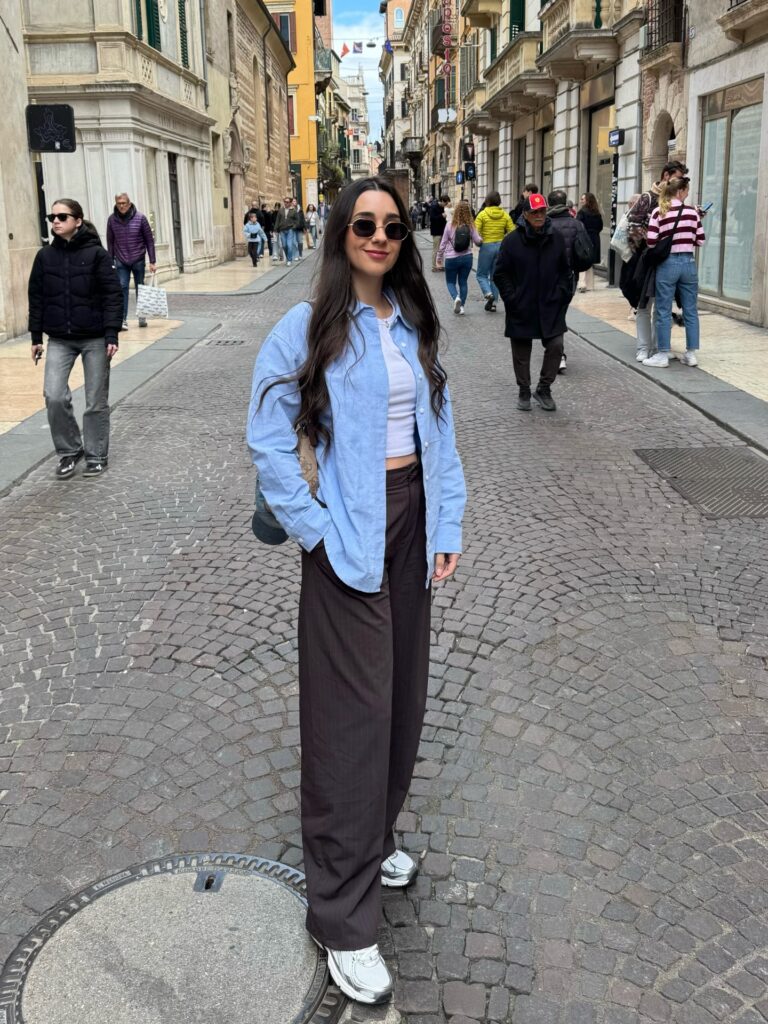 Light blue oxford shirt over a white top with brown pinstripe wide-leg trousers and silver sneakers in Verona