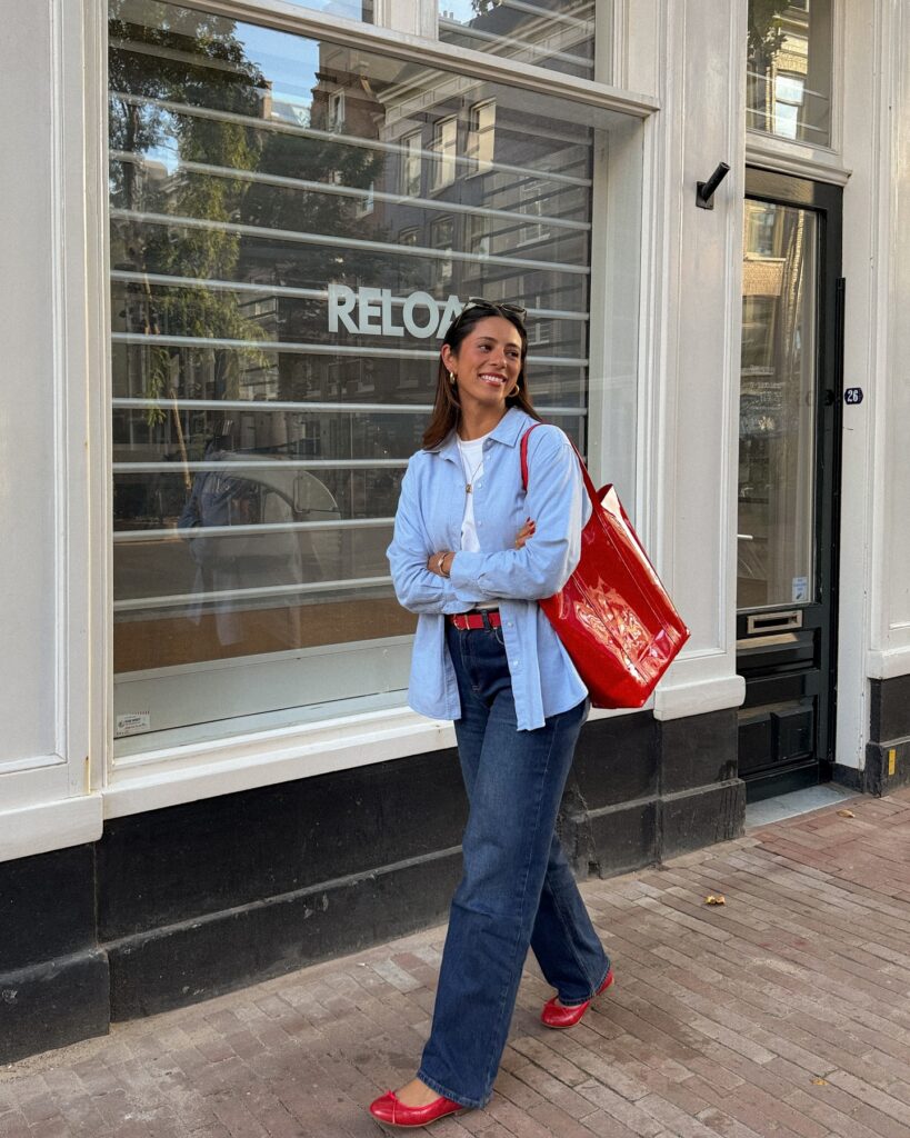 Light blue oxford shirt with a white tee, dark jeans, red ballet flats and a red patent tote in Amsterdam