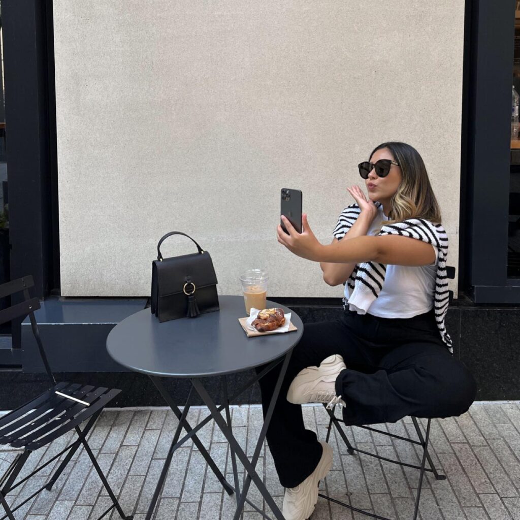 White tee with a black-and-white striped sweater tied over the shoulders, black trousers and chunky sneakers at a café