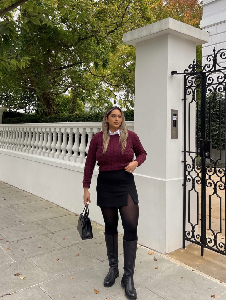 Burgundy cable-knit sweater over a white collared shirt with a black mini skirt, sheer tights and black knee-high boots