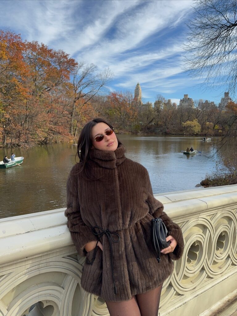 Brown faux-fur coat with black tights and a black clutch on a Central Park bridge