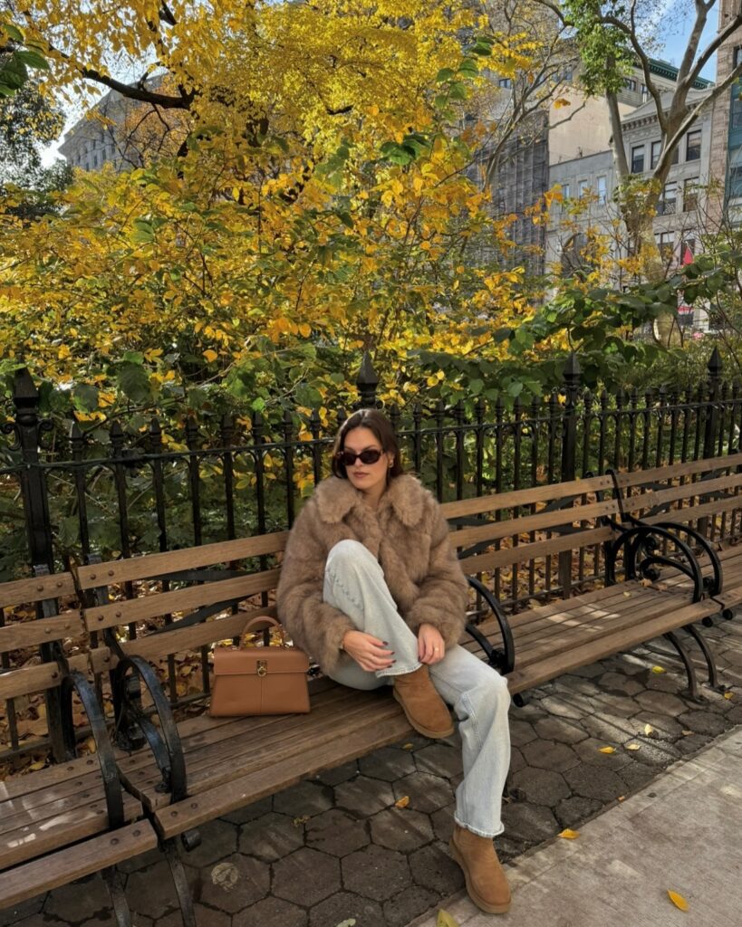 Taupe faux-fur jacket with light-wash jeans and tan suede boots among yellow autumn leaves