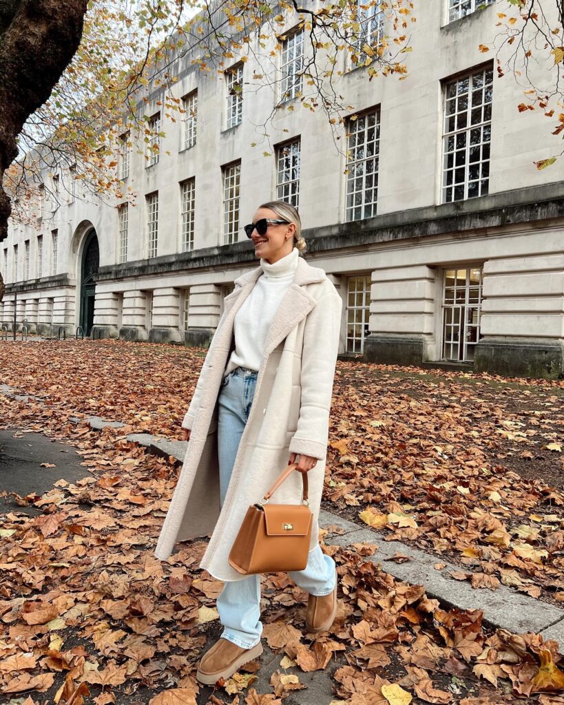 Cream shearling longline coat over a white turtleneck and light jeans with tan platform boots and a tan top-handle bag