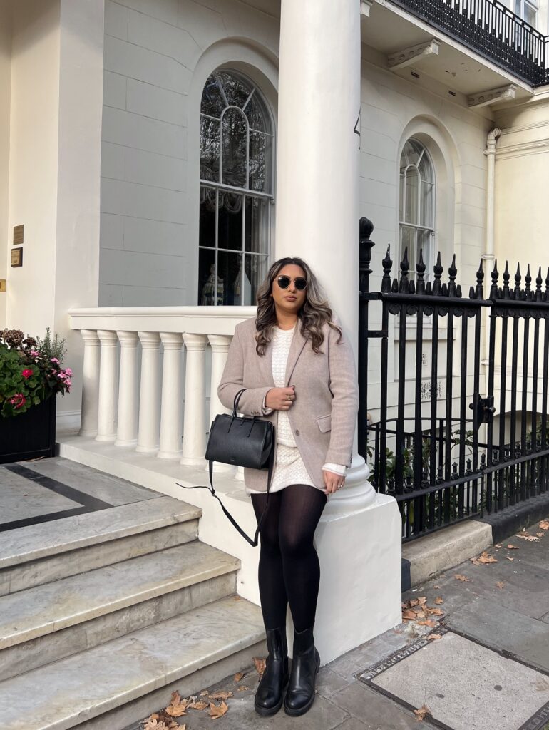 Oatmeal blazer over a cream knit mini dress with black tights, black ankle boots and a black bag