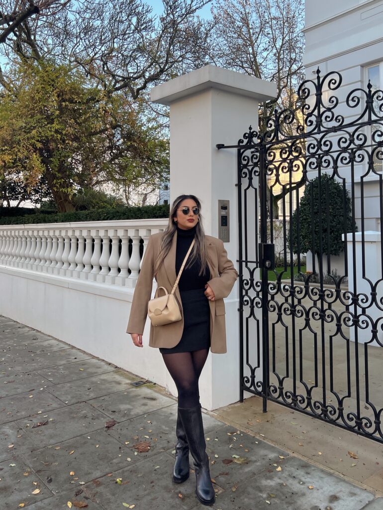 Camel blazer with a black turtleneck and black mini skirt, sheer tights, black knee-high boots and a cream bag
