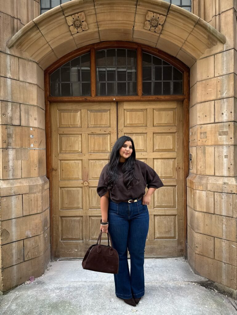 Brown short-sleeve knit top and dark-wash flared jeans with a brown belt and brown bag