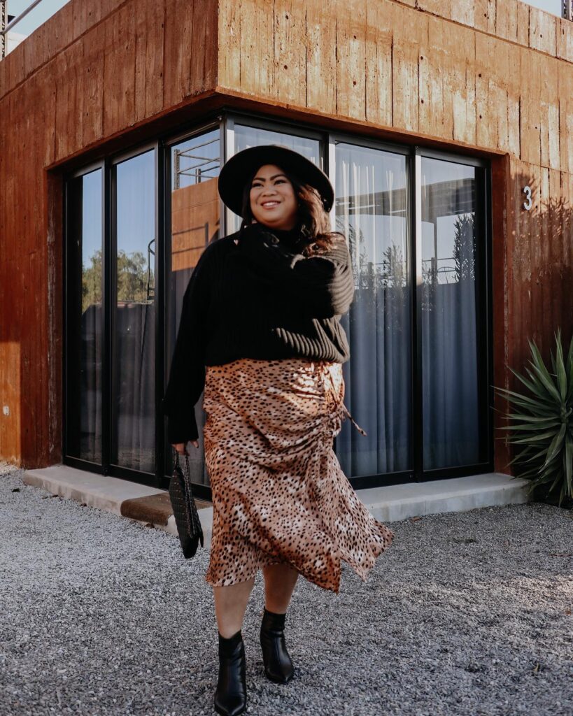 Black turtleneck sweater with a leopard-print ruched midi skirt, a black wide-brim hat and black ankle boots