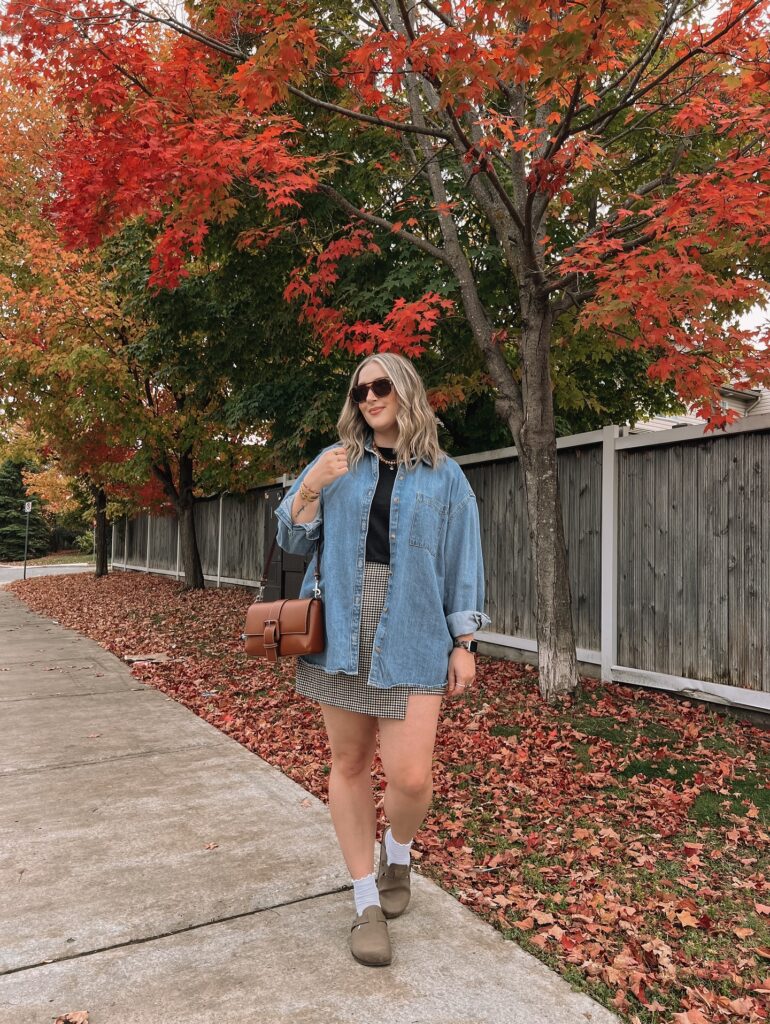 Oversized denim shirt over a black top with a black-and-white gingham mini skirt, white socks and brown clogs