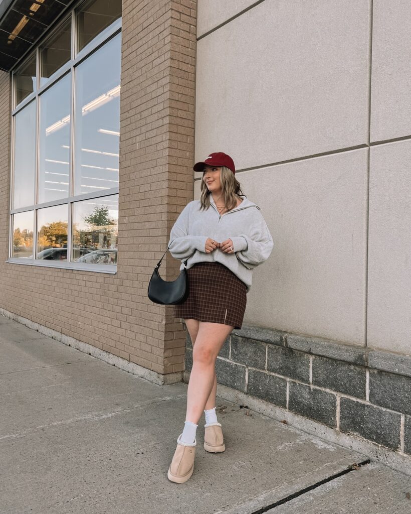 Grey quarter-zip sweater with a brown plaid mini skirt, a burgundy cap, tan mini boots and a black bag