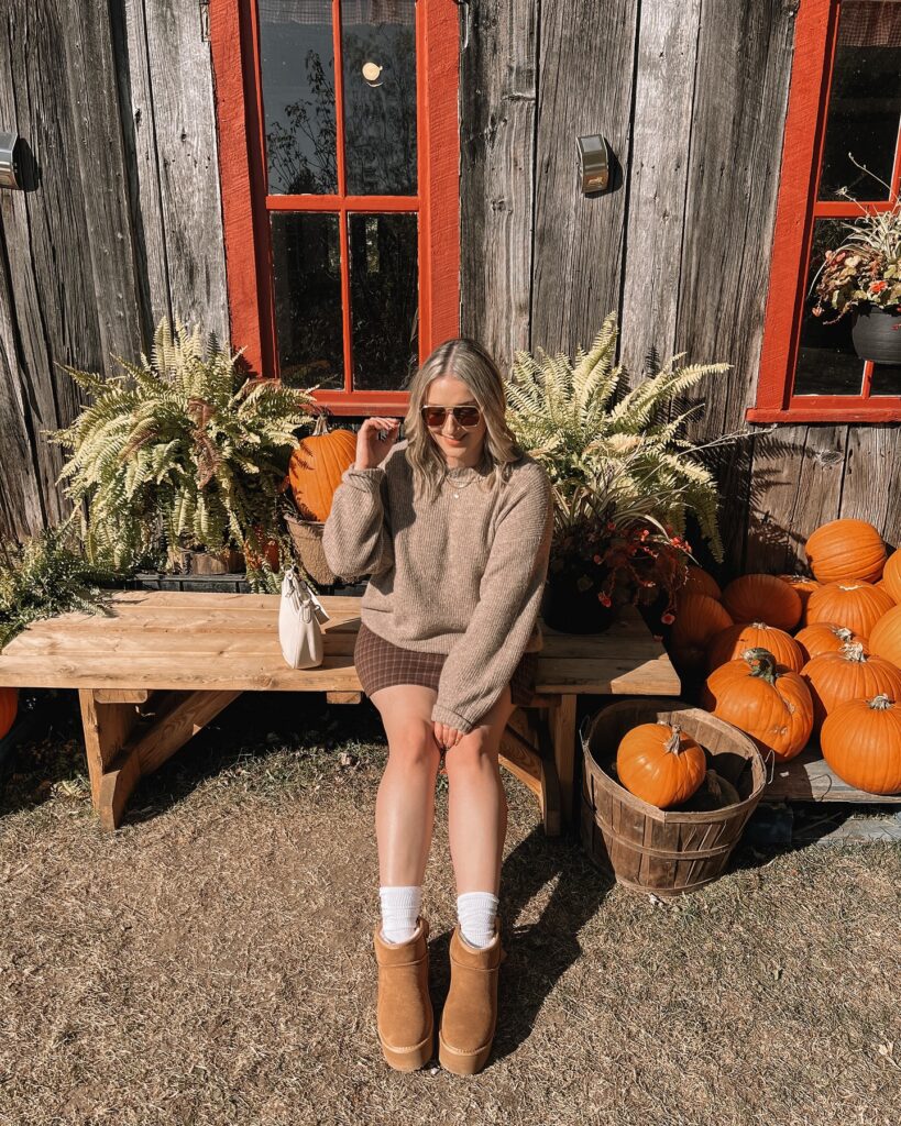 Oversized oatmeal sweater with a plaid mini skirt, white socks and tan platform boots, sitting by a pile of pumpkins