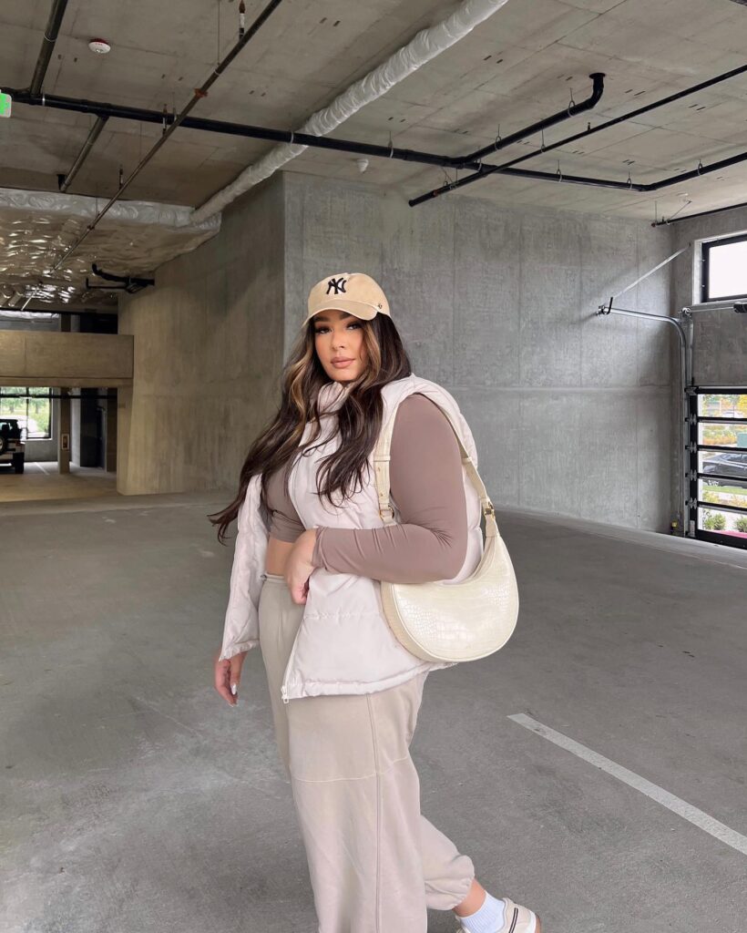 Cream puffer vest over a brown long-sleeve top with matching wide-leg sweatpants, a tan cap and a cream shoulder bag