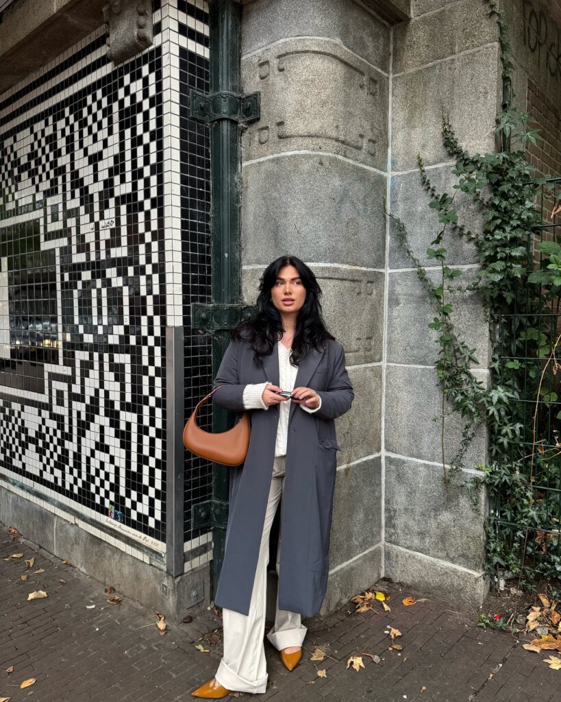 Grey longline coat over a white top and cream trousers with mustard pointed heels