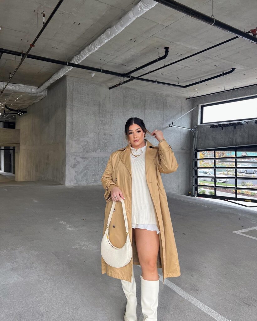 Camel trench coat over a cream ribbed knit dress with white knee-high boots