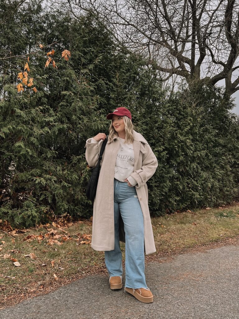 Long oatmeal wool coat over a graphic sweatshirt with light-wash wide-leg jeans, platform boots and a red cap