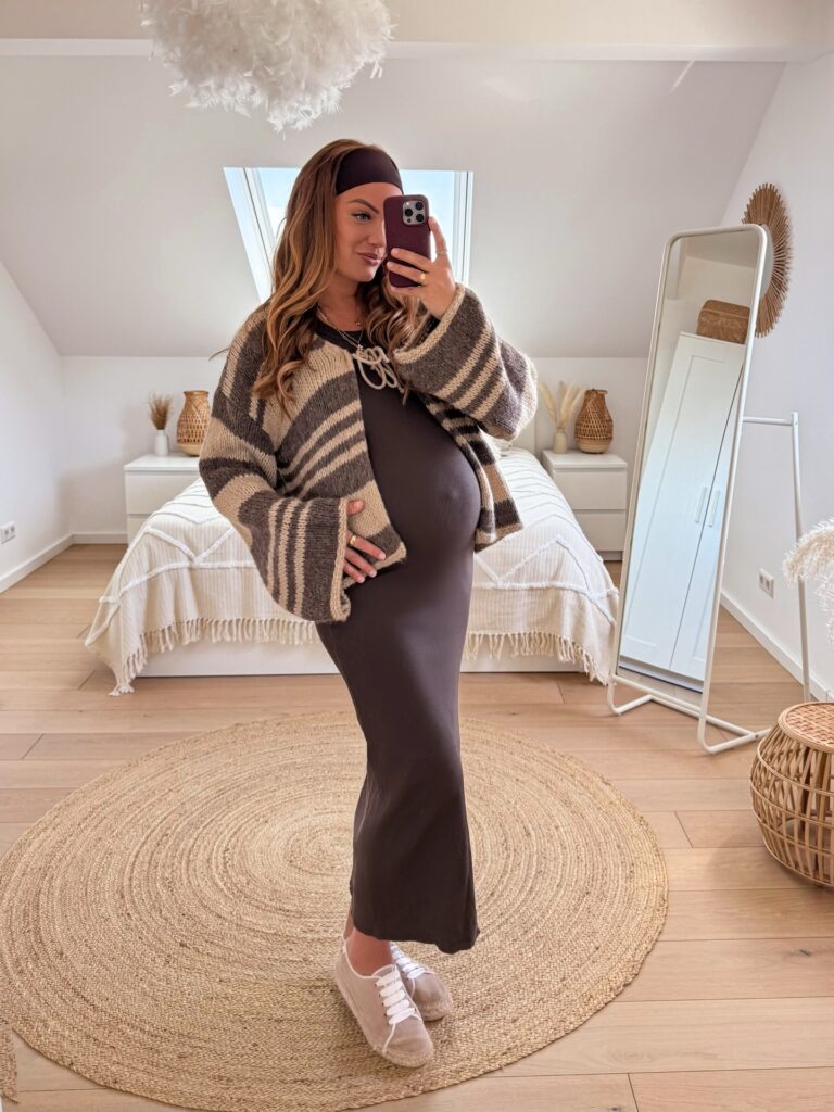 Pregnant woman in a grey and tan striped chunky cardigan over a brown bodycon maxi dress with a matching headband