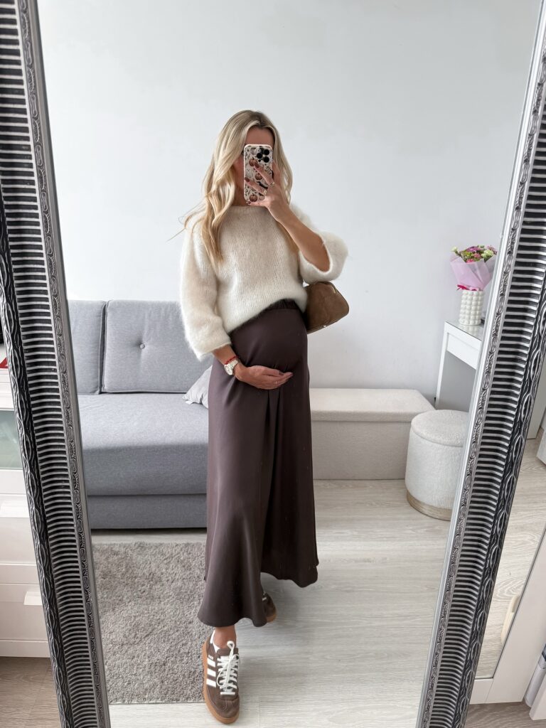 Pregnant woman in an ivory mohair sweater with a brown satin slip maxi skirt and brown Adidas Samba sneakers