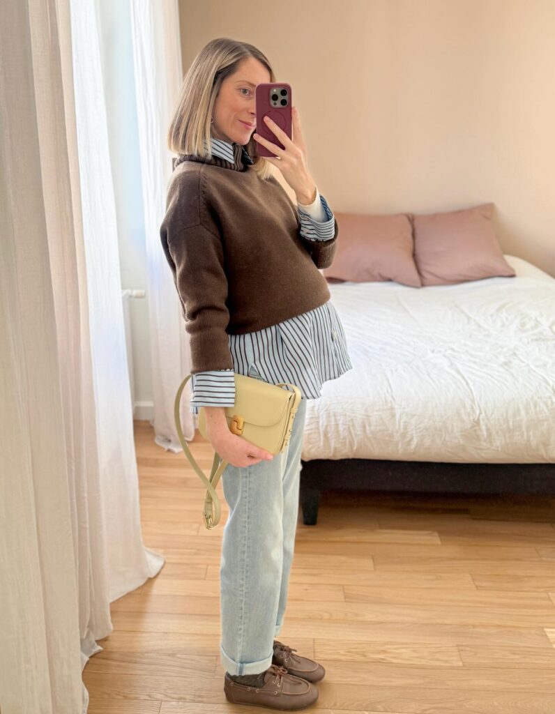 Pregnant woman in a khaki trench coat with a white tee, light wide-leg jeans and black loafers at a café table