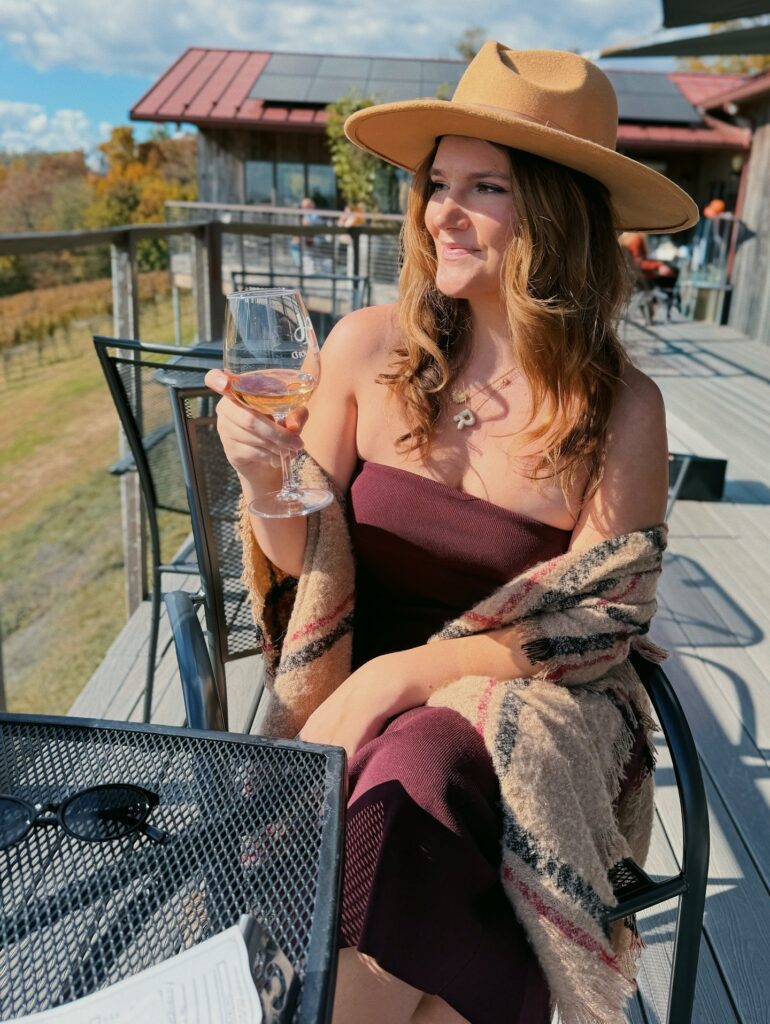 Woman in a burgundy strapless dress with a plaid blanket scarf and camel felt hat on a winery deck