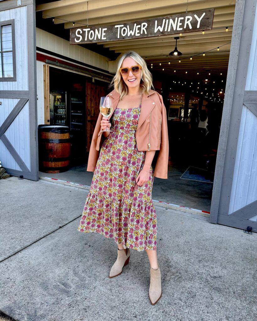 Woman in a floral midi dress with a tan leather moto jacket and suede booties at a winery