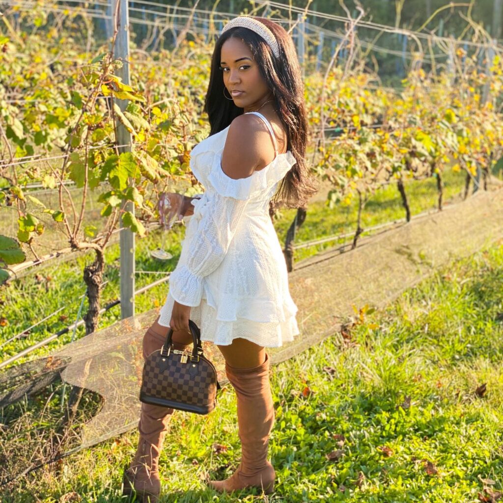 Woman in a white off-shoulder ruffle dress with tan suede over-the-knee boots in a golden vineyard