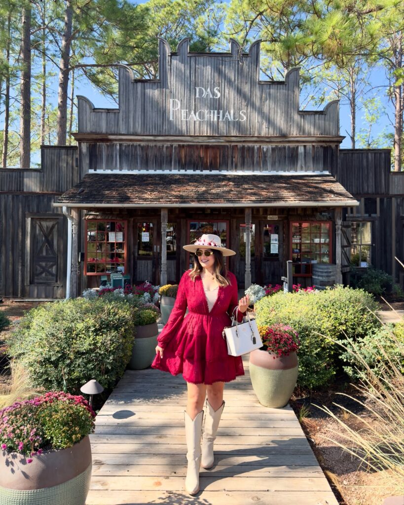 Woman in a red lace mini dress, cream felt hat and white western boots on a wooden walkway