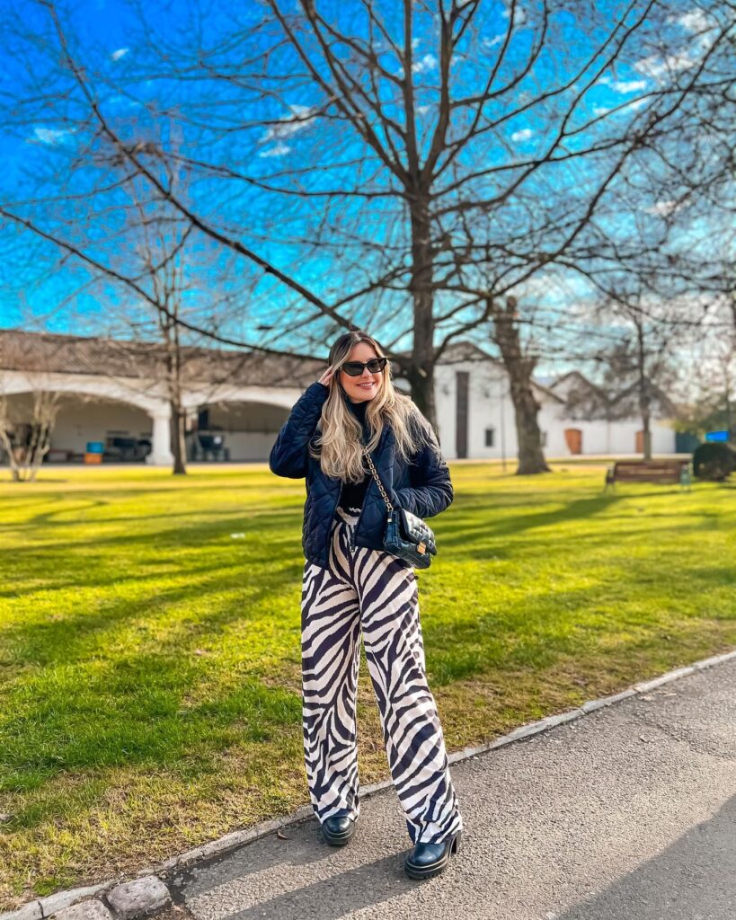Woman in a navy quilted jacket, printed wide-leg trousers and black boots on a tree-lined path