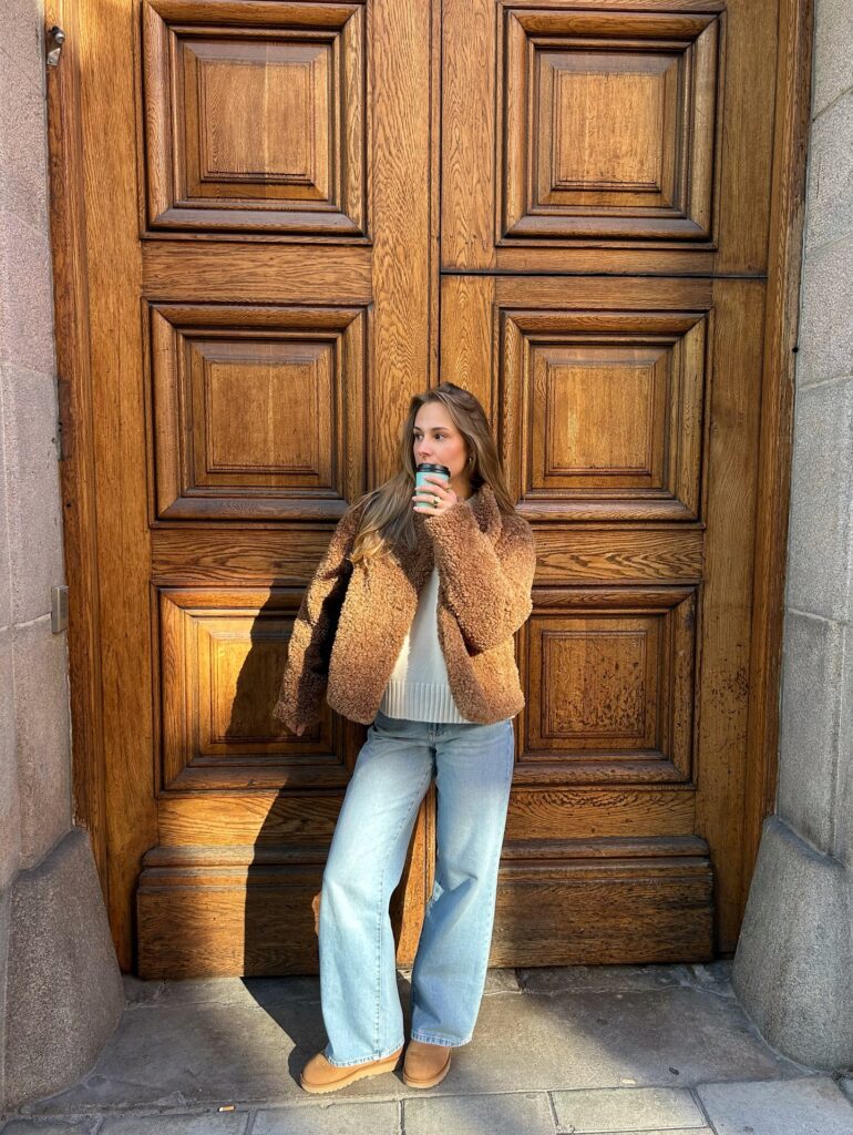 Brown teddy shearling jacket over a cream knit with light-wash wide-leg jeans and chestnut UGG mini boots