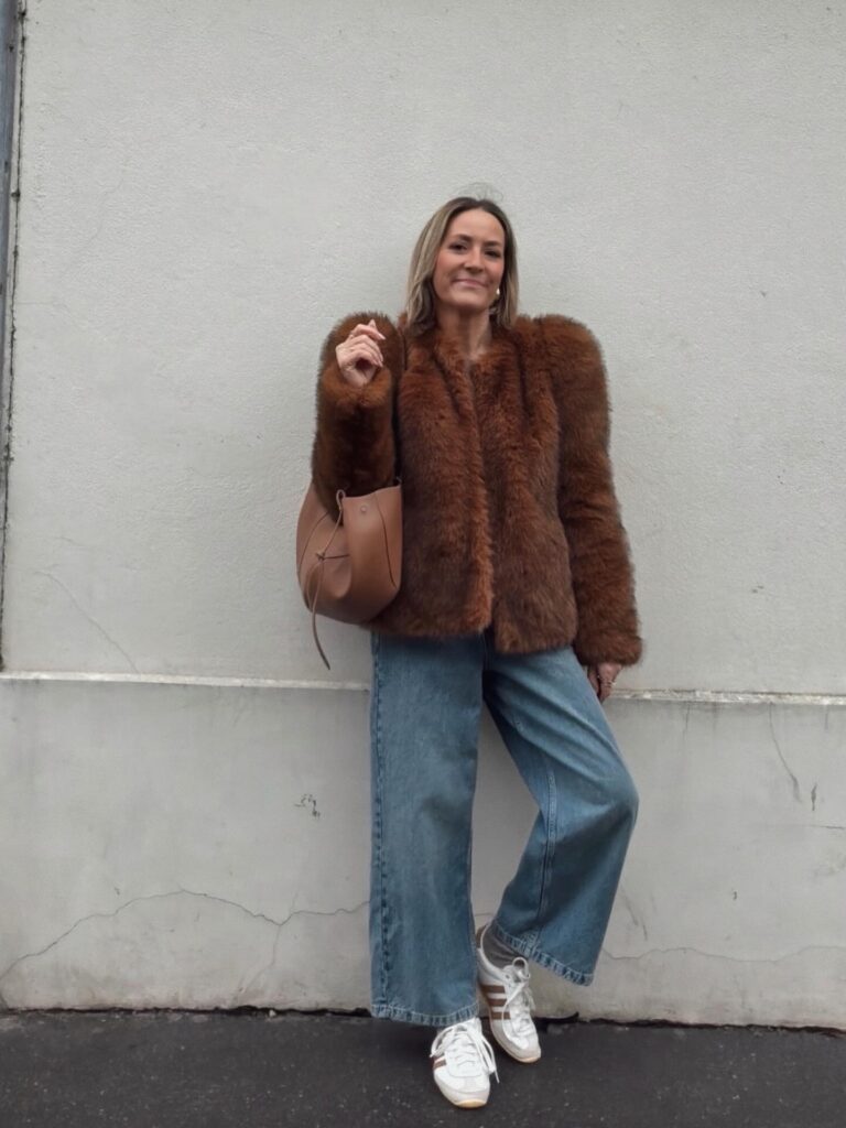 Rich brown faux-fur jacket with light-wash jeans, white Adidas sneakers and a tan bucket bag