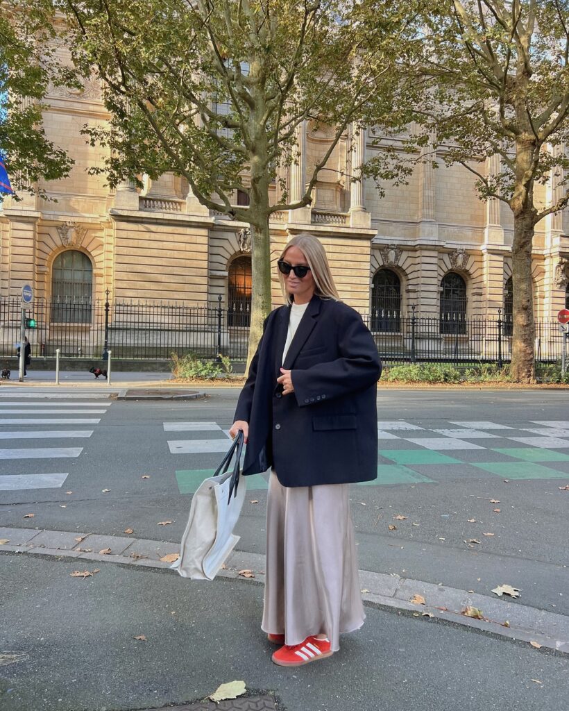 Navy oversized blazer over a champagne satin maxi skirt with red Adidas Gazelle sneakers and a canvas tote