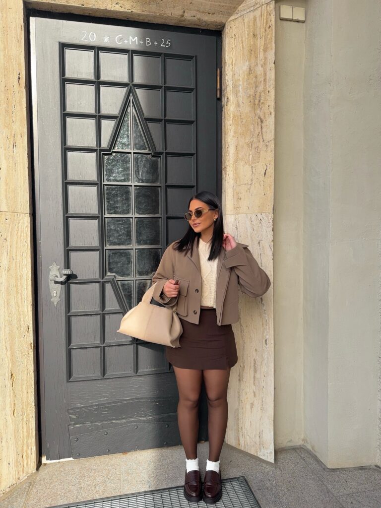 Taupe cropped jacket over a cream knit with a brown mini skirt and burgundy loafers