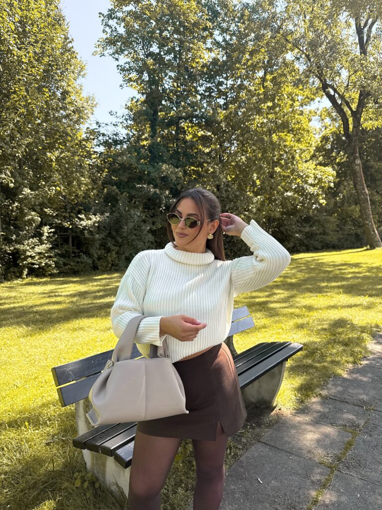 Cream turtleneck sweater with a brown mini skort, sheer tights and a taupe shoulder bag