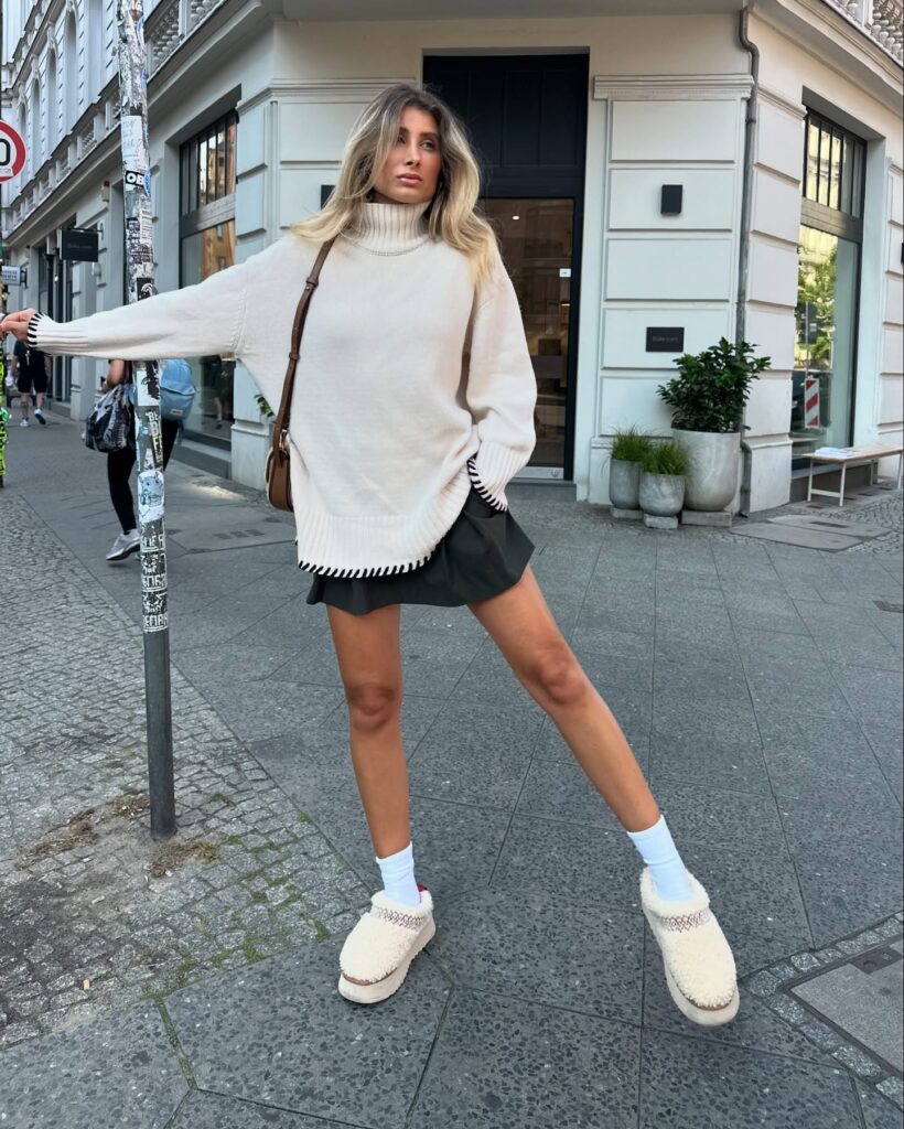 Cream oversized turtleneck sweater with an olive skort, white crew socks and cream shearling platform clogs