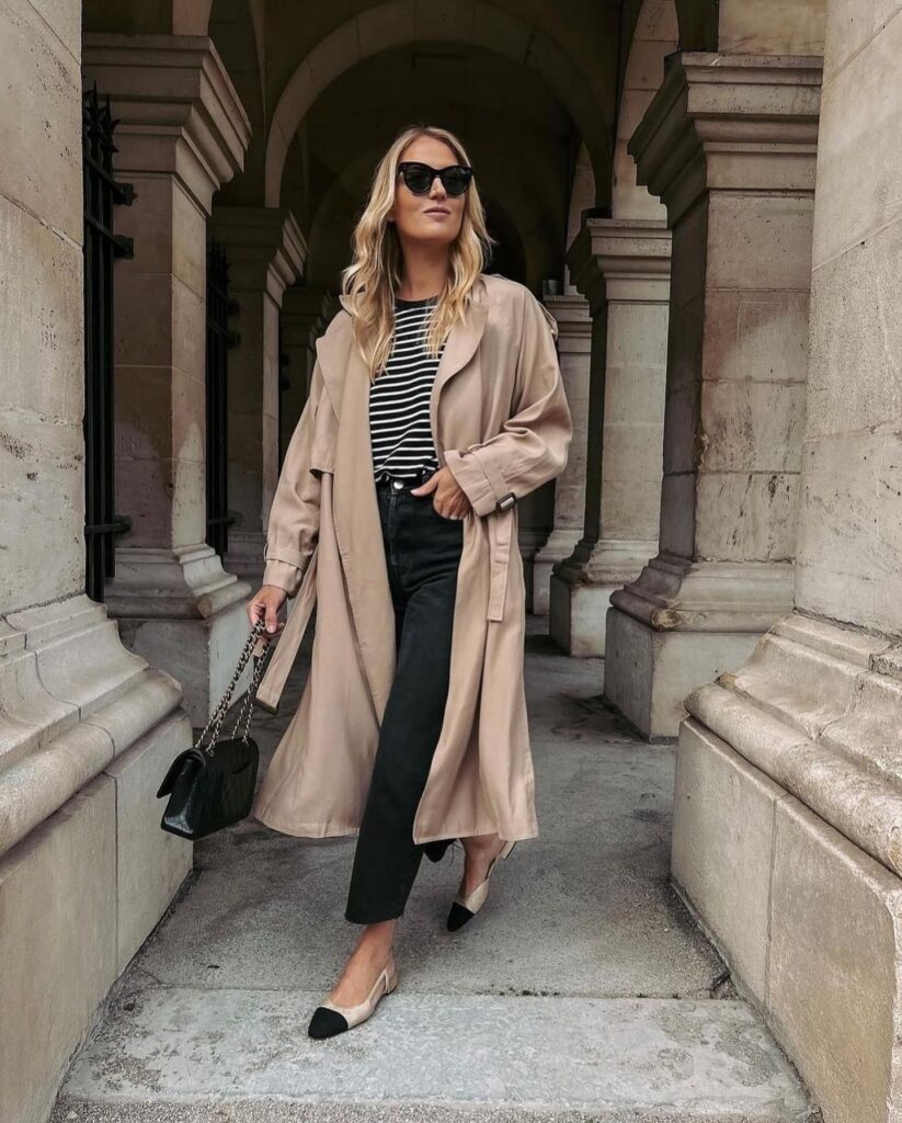 Camel trench coat over a Breton-striped top with black jeans and two-tone slingback flats
