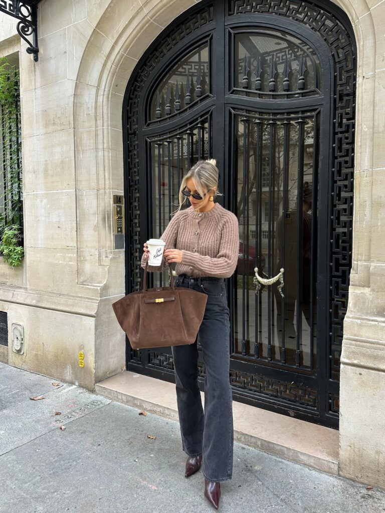 Woman in a taupe chunky knit cardigan with black wide-leg jeans, a brown suede tote and oxblood pointed boots in Paris
