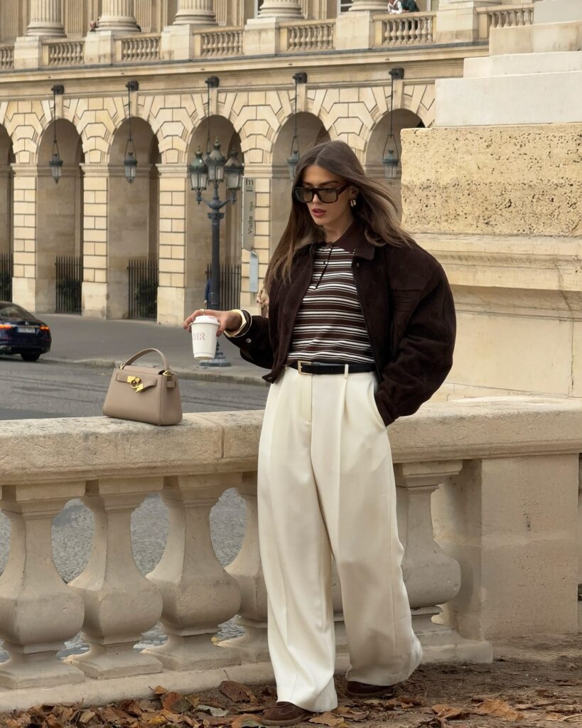 Woman in a neutral wool coat layered over soft knitwear with tailored trousers in an autumn setting