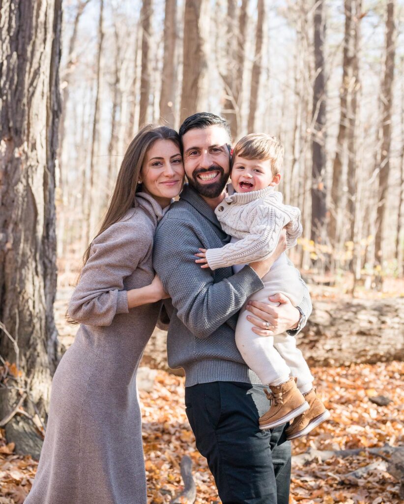 Couple holding toddler in soft taupe knits in winter woods