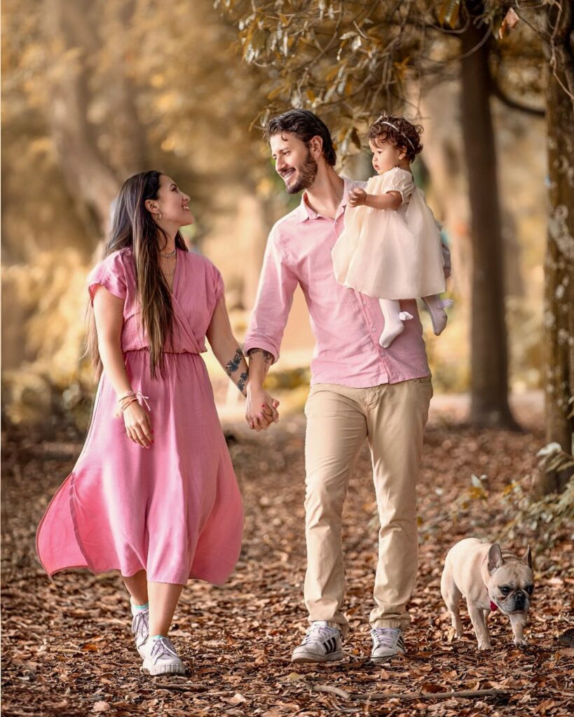 Couple with toddler and French bulldog walking in golden woods, all pink