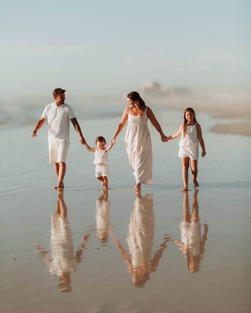 Family of four walking on the beach in all white, reflection in the sand