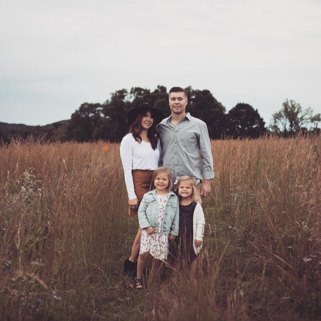 Family in tall grass, mom in white top and rust skirt with a hat