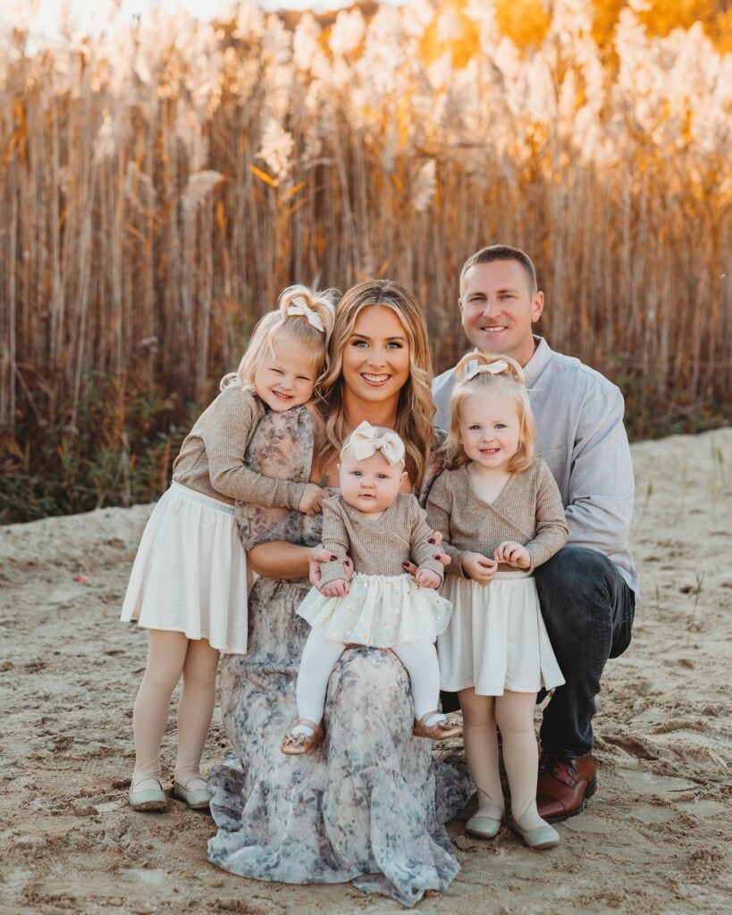 Family of five on sandy ground by reeds, taupe florals and cream
