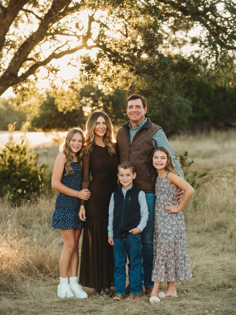 Family of five under an oak at sunset, mom in brown maxi