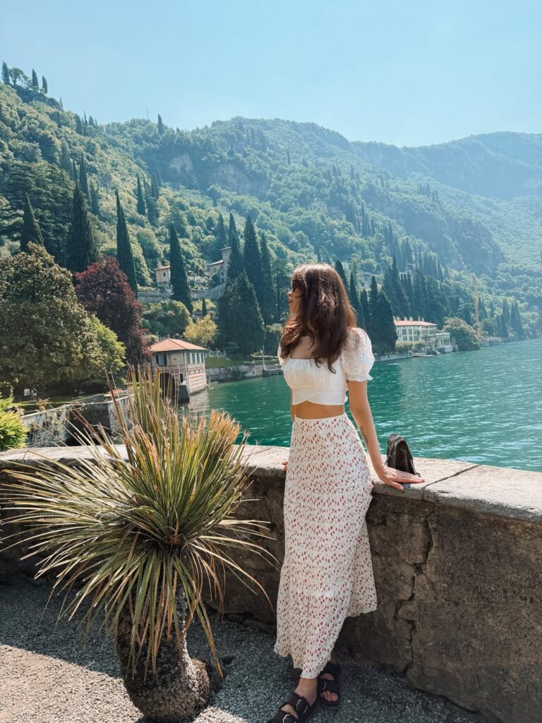 Woman in a white puff-sleeve crop top and red ditsy floral maxi skirt with sandals overlooking Lake Como in Varenna