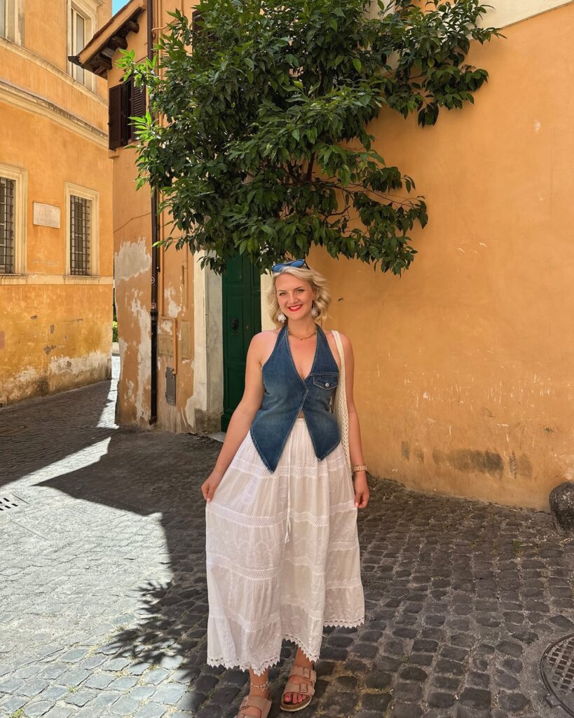 Woman wearing a denim halter vest and white embroidered prairie maxi skirt with Birkenstocks on a cobblestone street in Rome