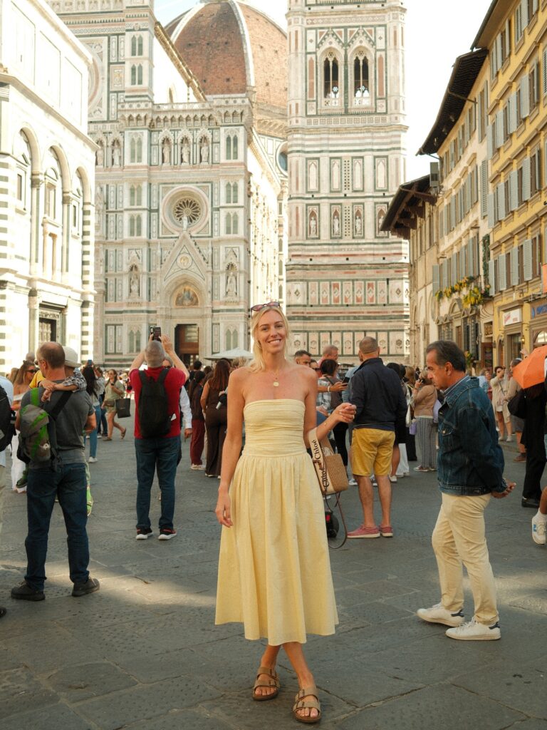 Woman in a soft yellow strapless midi dress and suede buckle sandals standing in front of the Duomo in Florence