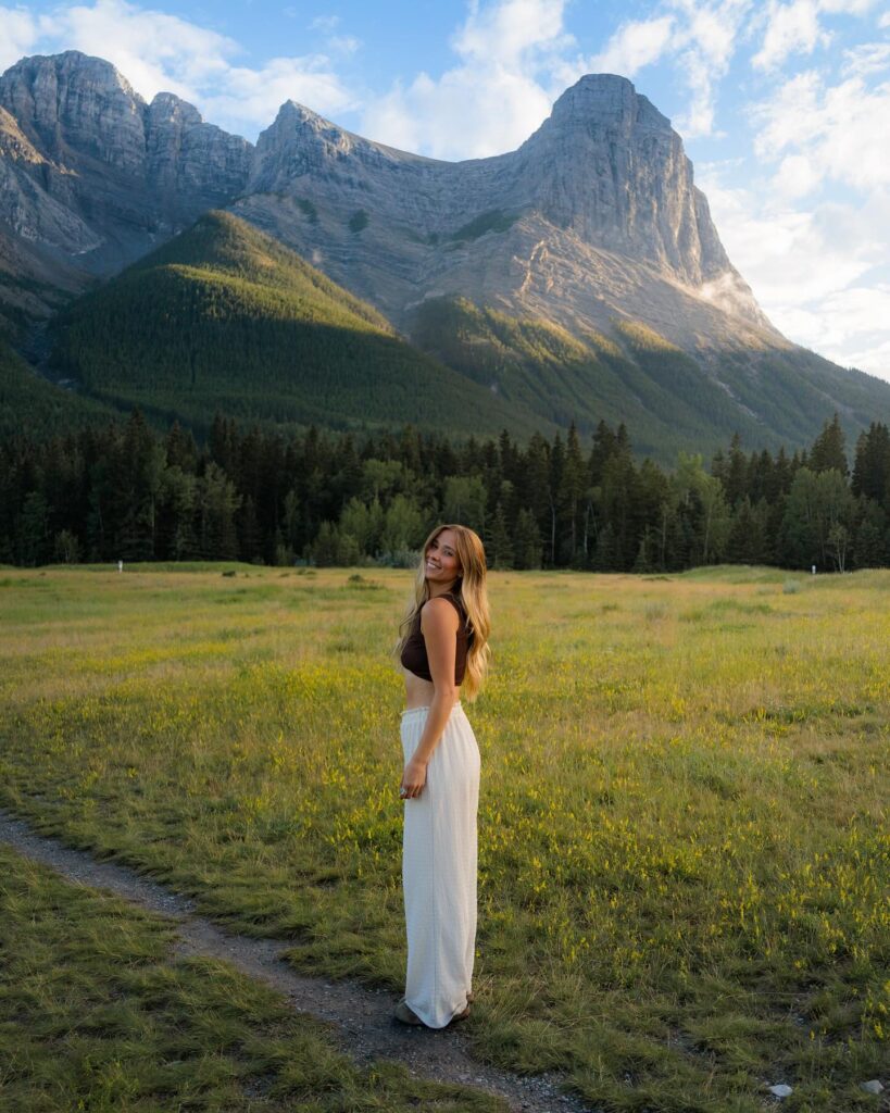 Woman wearing a brown cropped tank top and cream wide-leg pants standing in a mountain meadow at golden hour