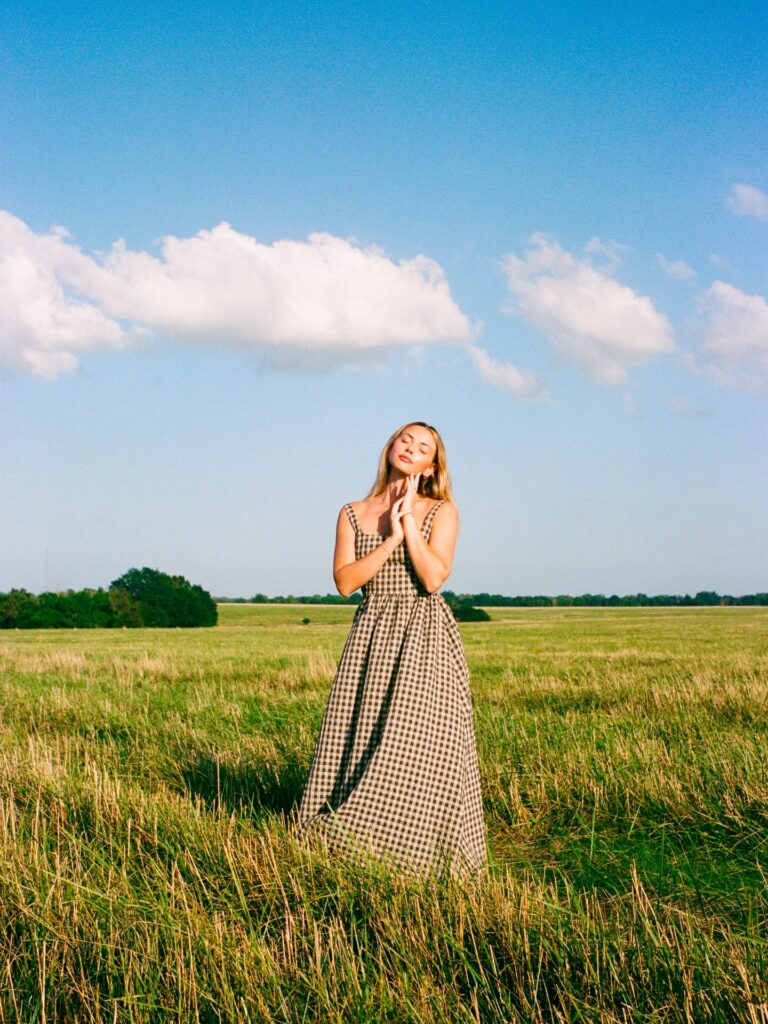 Woman wearing a black and cream gingham maxi dress standing in a wide open grassy field under a blue sky